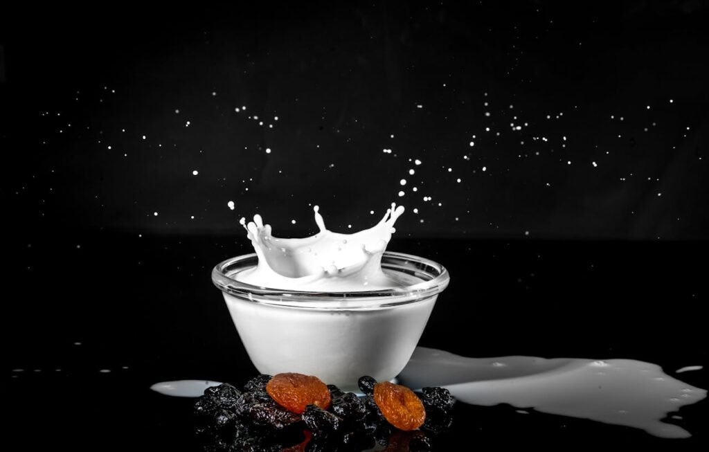 Dramatic milk splash in glass bowl with raisins and apricots on black background.